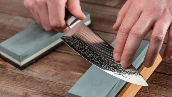 A photograph of a person sharpening a traditional Gyuto knife using a whetstone