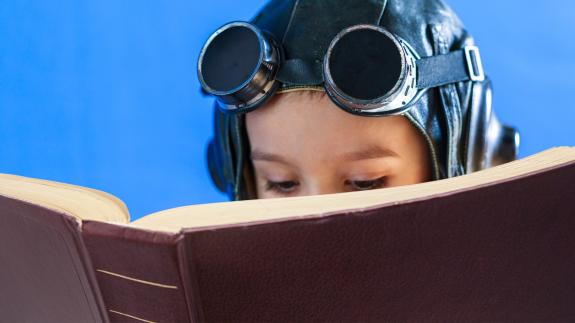 A child reading a book while wearing pilot's headgear