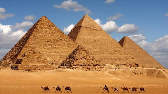 Camels walk in front of the three pyramids in the Giza Pyramid Complex