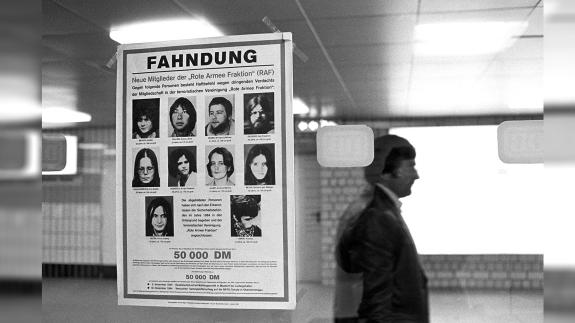 Black and white photograph showing poster in a German train station appealing for help in the capture of the Baader-Meinhog gang members