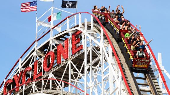 People raise their hands as they ride the Cyclone rollercoaster in Coney Island