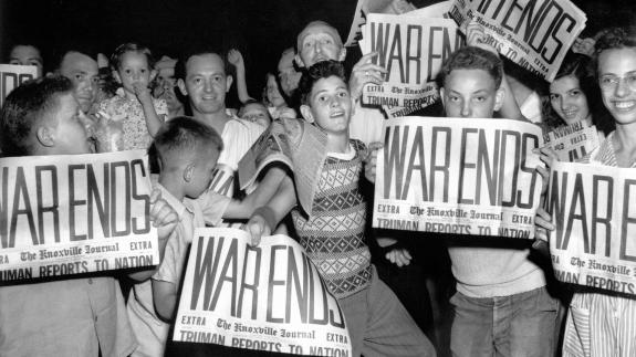 Young people in the US celebrate VJ Day while holding newspapers with the headline 'WAR ENDS'