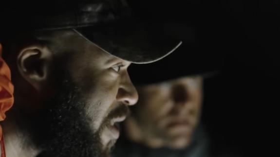 Kru Williams inside a cave - the side profile of his face is visible and lit up by torch light. To his side, out of focus, is Adam Palmer