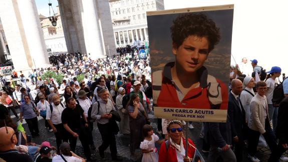 A woman in a crowd holds a sign of Carlo Acutis' face during his canonisation in Vatican City