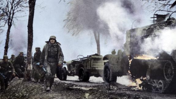Colourised image of German soldiers passing burning U.S. equipment in the beginning of the Battle of the Bulge