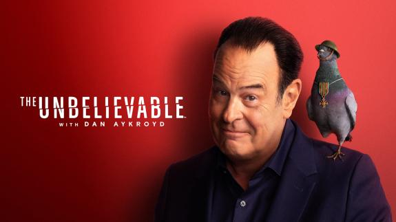 Dan Aykroyd next to the show title with a one-legged pigeon standing on his shoulder. The pigeon is wearing a WWI helmet and has a military medal around its neck