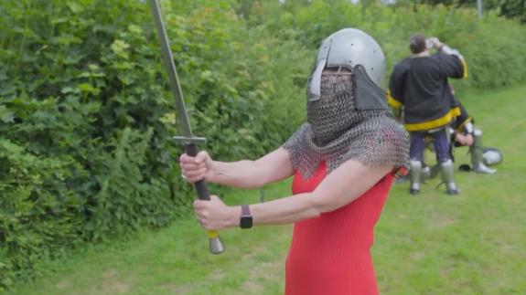 Professor Alice Roberts wearing a medieval helmet and holding a large sword
