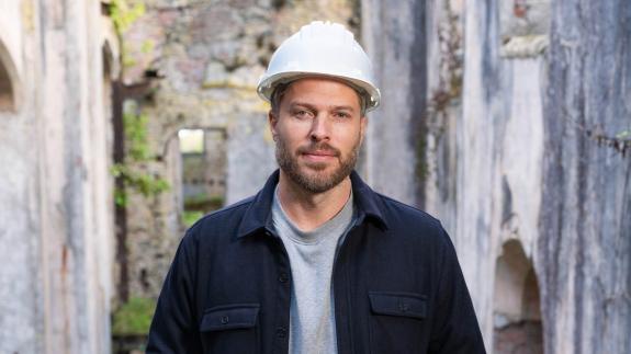 Rick Edwards wearing a white hard hat in the ruins of a castle