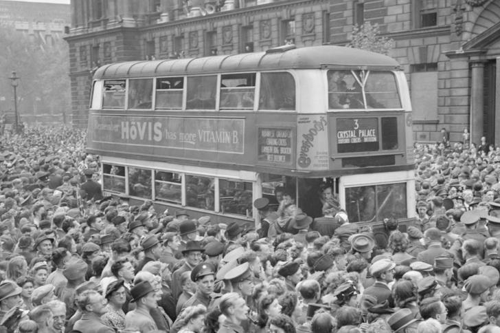 People in London crowd the streets and surround a double-decker bus on VE Day 1945