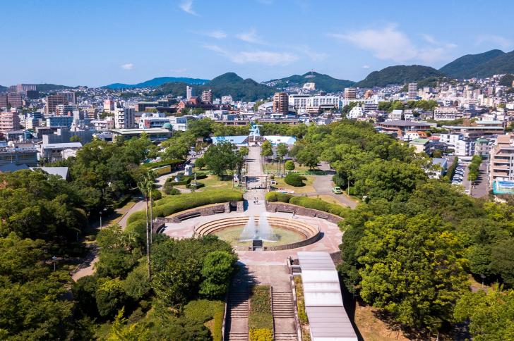 High angle view of Nagasaki Peace Park in Japan. Scenery consist of statues, many buildings, blue sky with cloud and green trees.