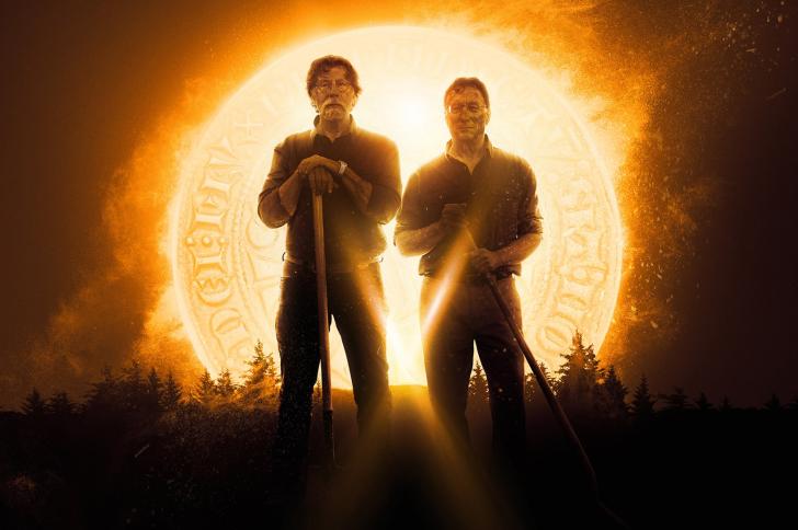 Rick and Marty Lagina hold shovels while standing in front of a glowing golden coin