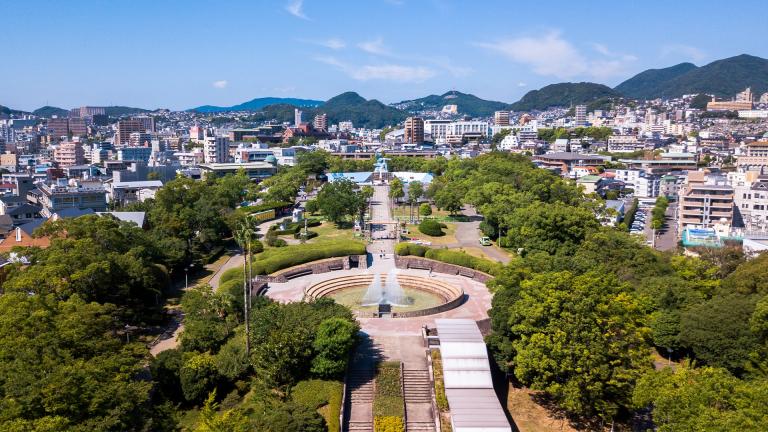 High angle view of Nagasaki Peace Park in Japan. Scenery consist of statues, many buildings, blue sky with cloud and green trees.