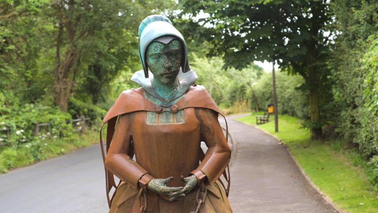 A copper statue depicting a woman in chains dressed in 16th/17th century clothes