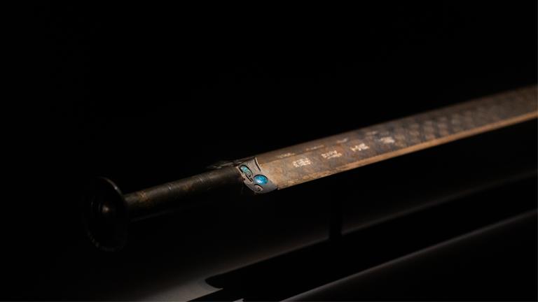 The Sword of Goujian on display in a museum against a black backdrop