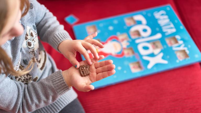 A little girl holding a chocolate that she has just got from her advent calendar. The advent calendar is on the table in the background